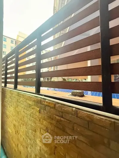 Modern apartment balcony with wooden railing and brick wall overlooking pool area.