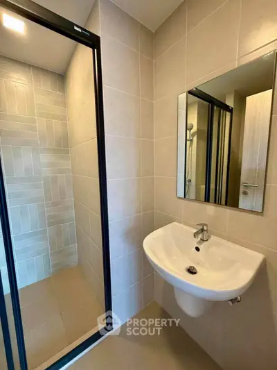Modern bathroom with sleek sink and glass shower enclosure in contemporary apartment.