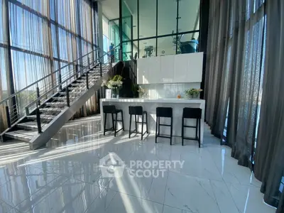 Luxurious modern kitchen with high ceilings and sleek design, featuring a stylish staircase and large windows.