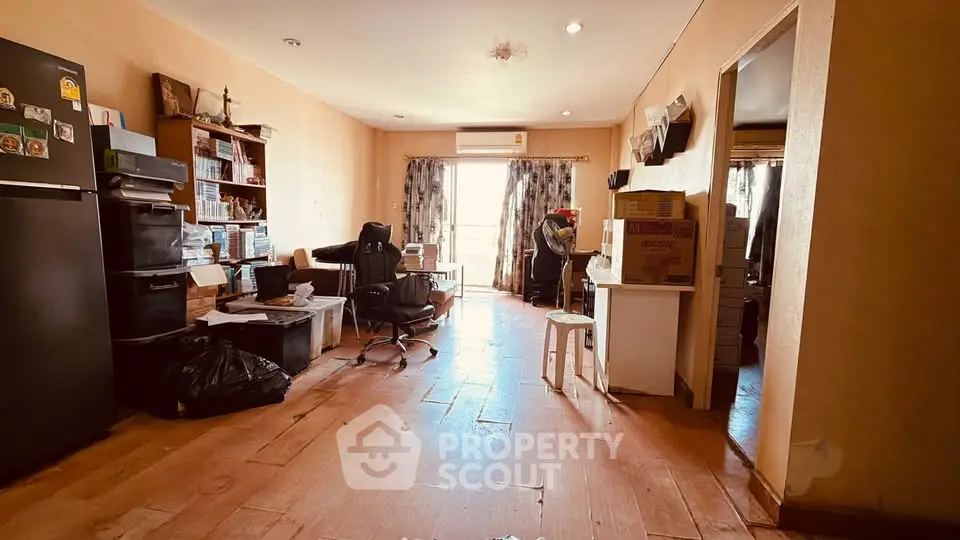 Spacious living room with natural light, featuring a work area and modern furnishings, ideal for urban living.
