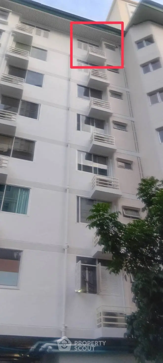 Modern multi-story residential building with small balconies and lush greenery