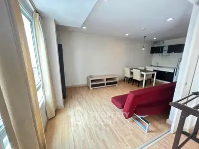 Modern open-plan living room with kitchen, featuring wooden flooring and a red sofa.