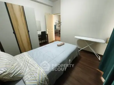 Cozy bedroom with single bed, ironing board, and wooden flooring