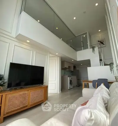 Spacious modern living room with high ceiling and mezzanine, featuring elegant decor and natural light.
