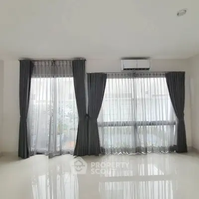 Spacious living room with large windows and elegant curtains, perfect for natural light and modern living.