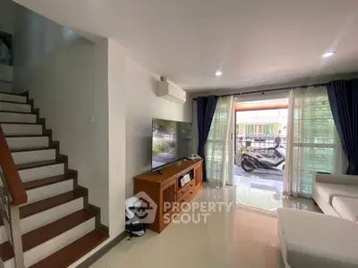 Modern living room with large TV and staircase, featuring natural light and sleek design.