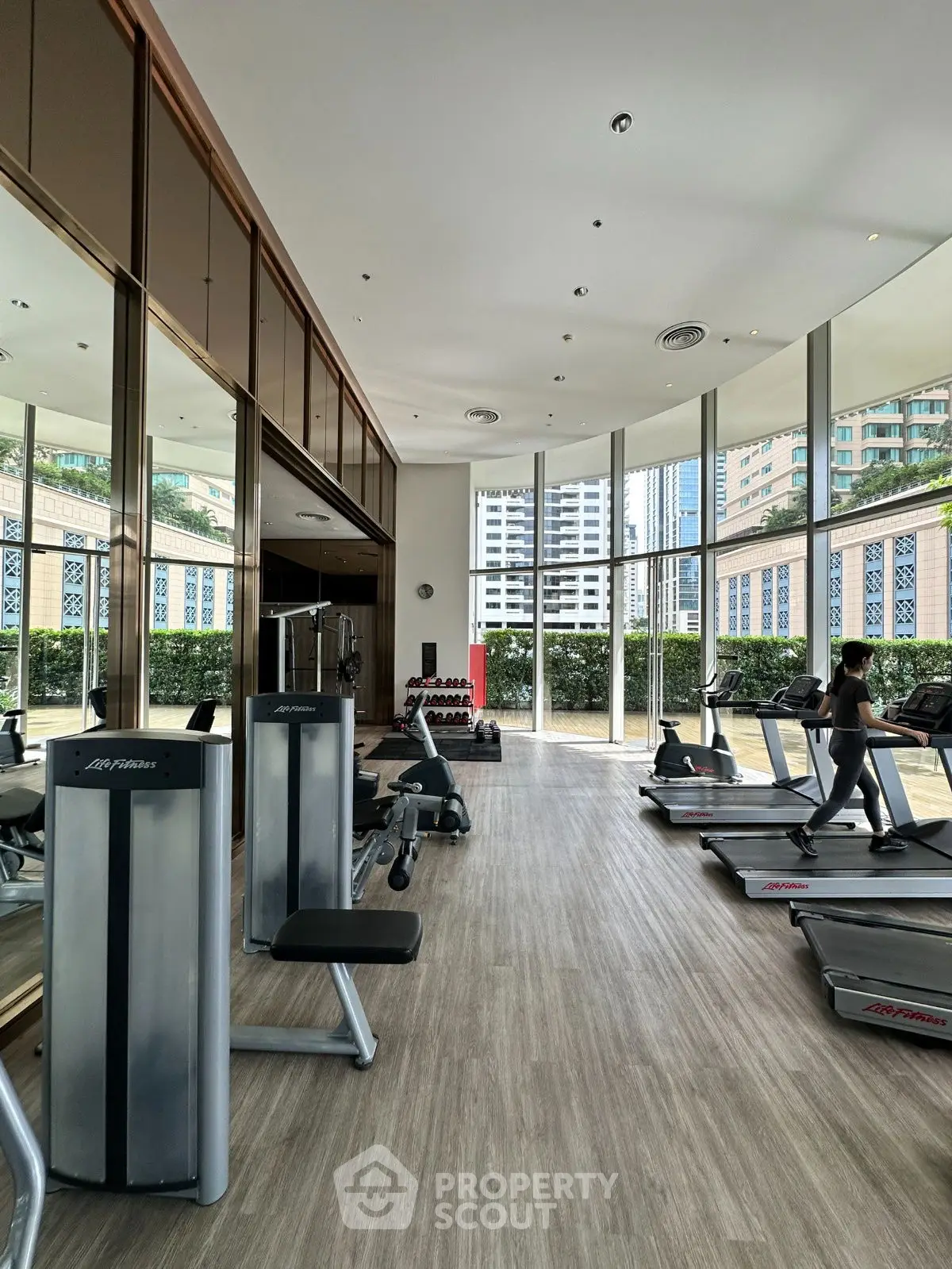 Spacious gym with modern equipment and large windows offering city views.