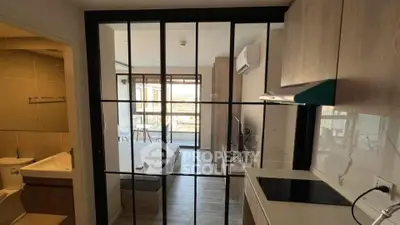 Modern studio apartment with glass partition, cozy bedroom, and sleek kitchen.