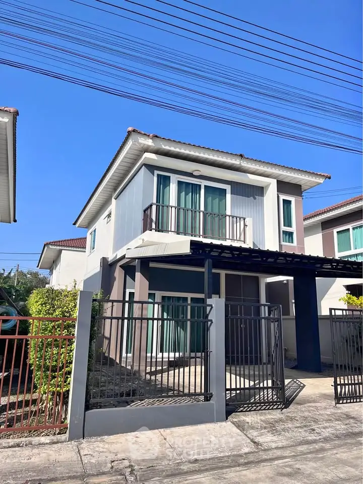 Charming two-story house with balcony and gated entrance in a serene neighborhood.