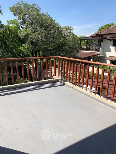 Spacious balcony with wooden railing and scenic view of lush greenery and neighboring homes.