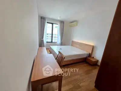 Spacious bedroom with wooden furniture and large window offering natural light.
