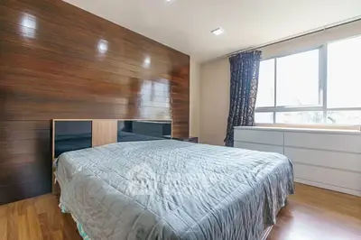 Spacious bedroom with wooden accent wall and large window for natural light.