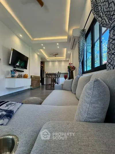 Modern living room with sleek design, featuring a large gray sofa, wall-mounted TV, and stylish lighting.
