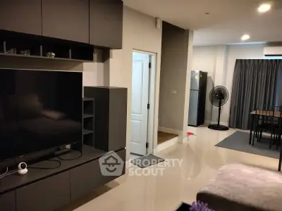 Modern living room with sleek furniture and open layout, featuring a large TV and dining area.