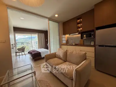 Modern open-plan living room with cozy sofa and kitchen, leading to a bedroom with a scenic view.
