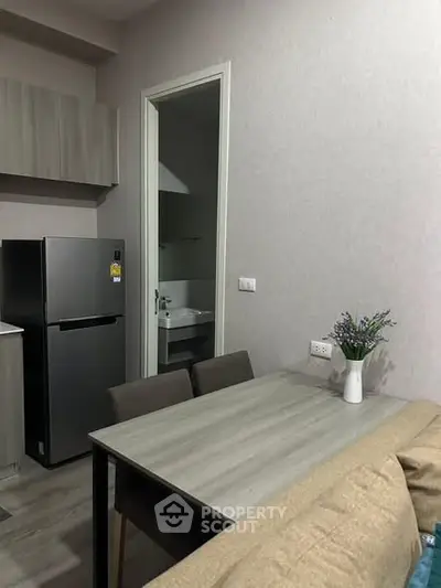 Modern compact kitchen with dining area and sleek refrigerator in cozy apartment.