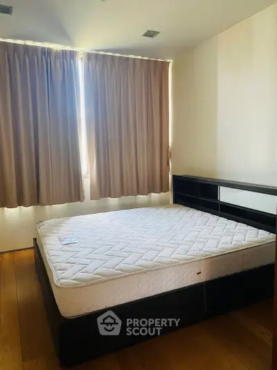 Spacious bedroom with large window and wooden flooring, featuring a comfortable bed and ample natural light.