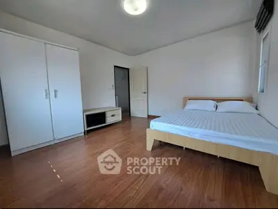 Spacious bedroom with wooden flooring and modern furniture in a bright apartment.
