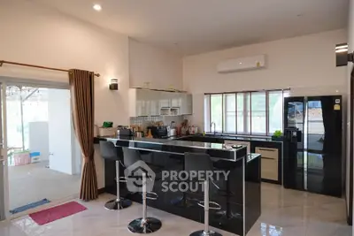 Modern kitchen with sleek black countertops and bar stools, featuring open layout and ample natural light.