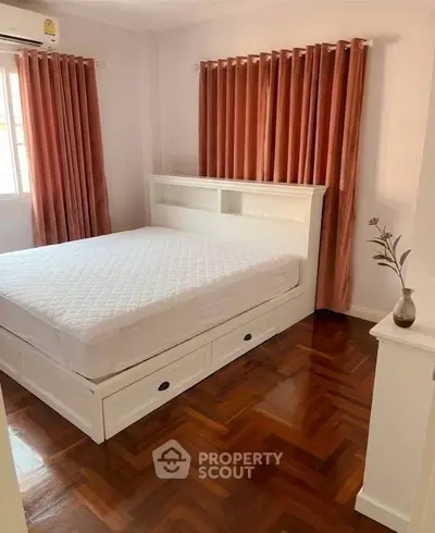 Cozy bedroom with elegant wooden flooring and ample natural light, featuring a stylish bed with storage drawers.