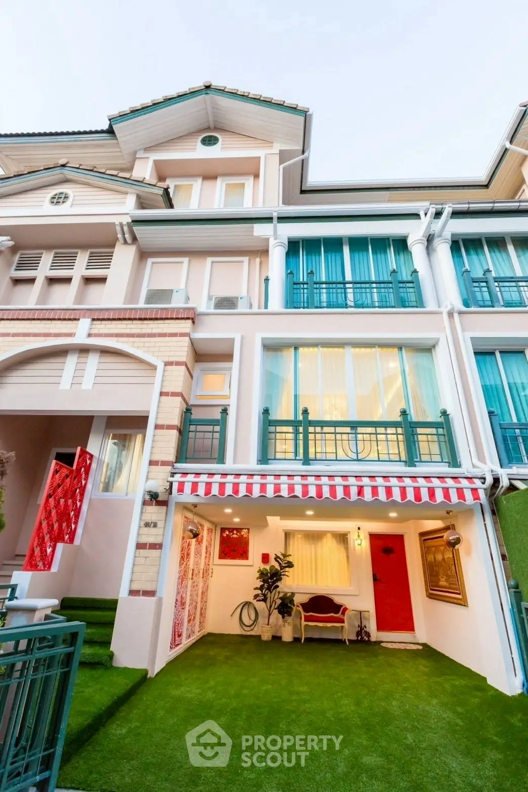Charming multi-story townhouse with vibrant facade and lush artificial grass lawn.