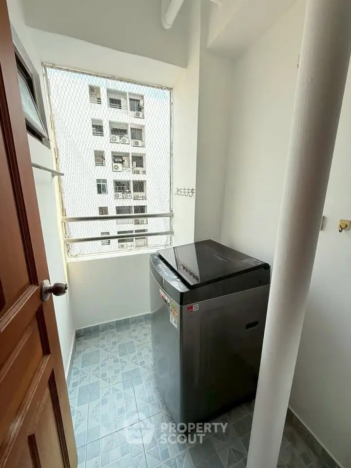 Compact laundry area with modern washing machine and tiled flooring in high-rise apartment.