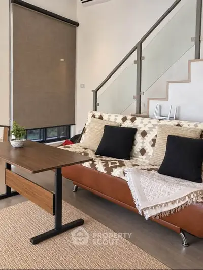 Modern living room with stylish sofa and staircase, featuring contemporary decor and natural light.