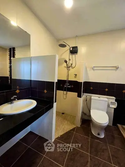 Modern bathroom with sleek black and white tiles, featuring a shower and toilet.