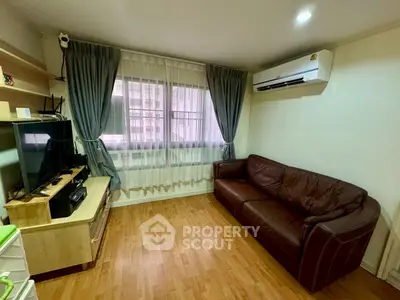 Cozy living room with leather sofa and entertainment center, featuring wooden flooring and air conditioning.