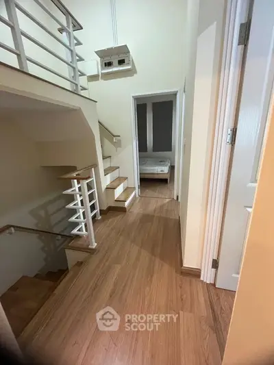 Spacious modern hallway with wooden flooring leading to a cozy bedroom, showcasing elegant staircase design.