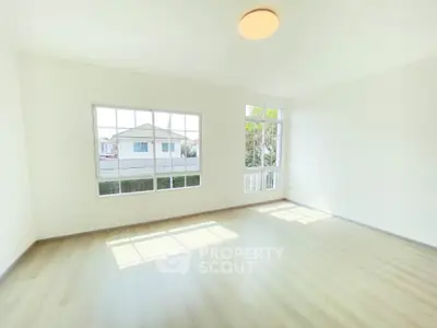 Spacious sunlit room with large windows and wooden flooring in modern home.