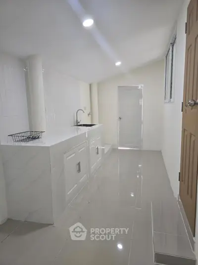 Sleek modern kitchen with glossy white cabinets and minimalist design, featuring a single sink and ample counter space.