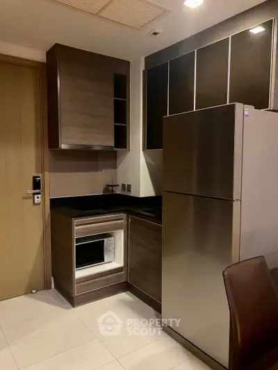 Modern kitchen with sleek cabinetry and stainless steel fridge in a compact layout.