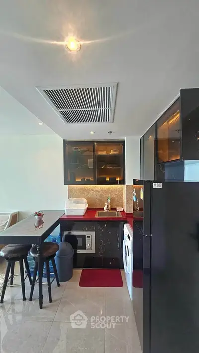 Modern kitchen with sleek black cabinets, washing machine, and breakfast bar seating.