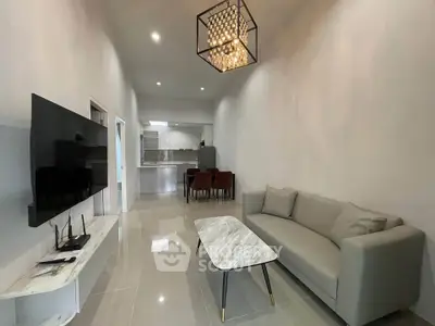 Modern living room with sleek furniture and open kitchen layout, featuring a stylish chandelier and glossy tile flooring.