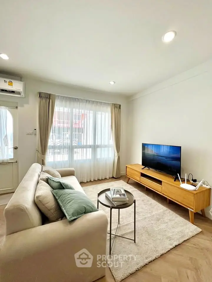 Modern living room with cozy sofa, TV, and natural light from large window.