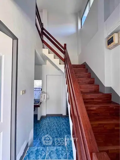 Charming staircase with wooden railing and vibrant blue flooring in a bright, airy home interior.