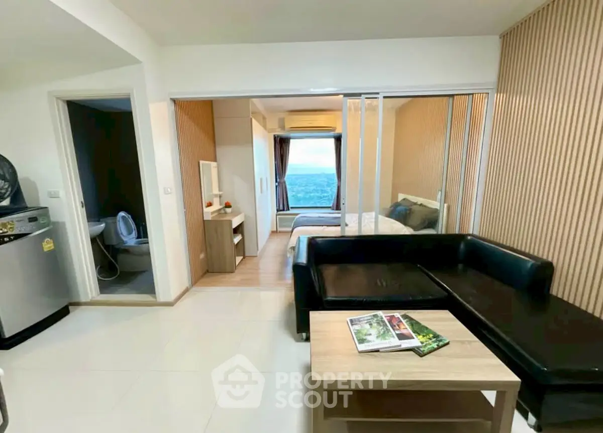 Modern studio apartment with ocean view, featuring sleek black sofa and compact kitchen area.