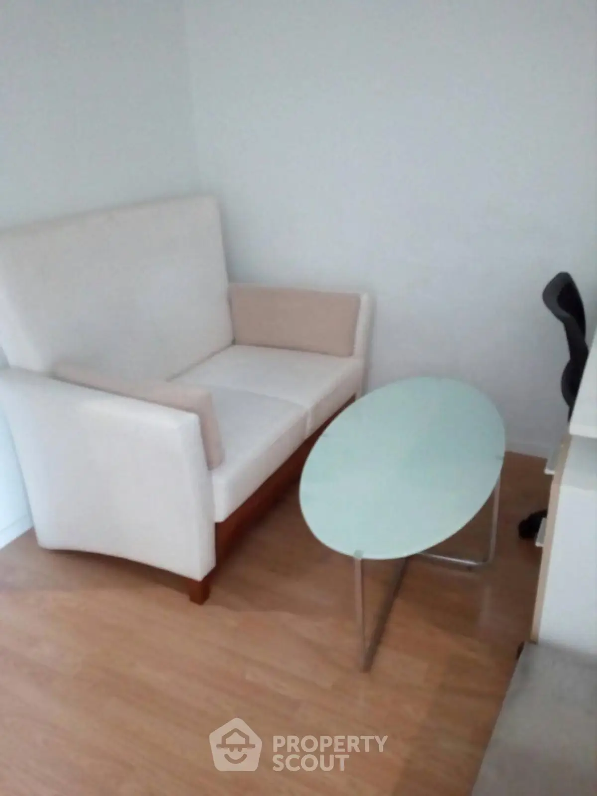 Cozy small living area with modern white sofa and glass coffee table on wooden floor.
