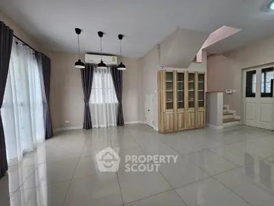 Spacious living room with gleaming tiled floors, elegant pendant lighting, and large windows draped in sheer curtains, complemented by a wooden bookshelf and staircase.