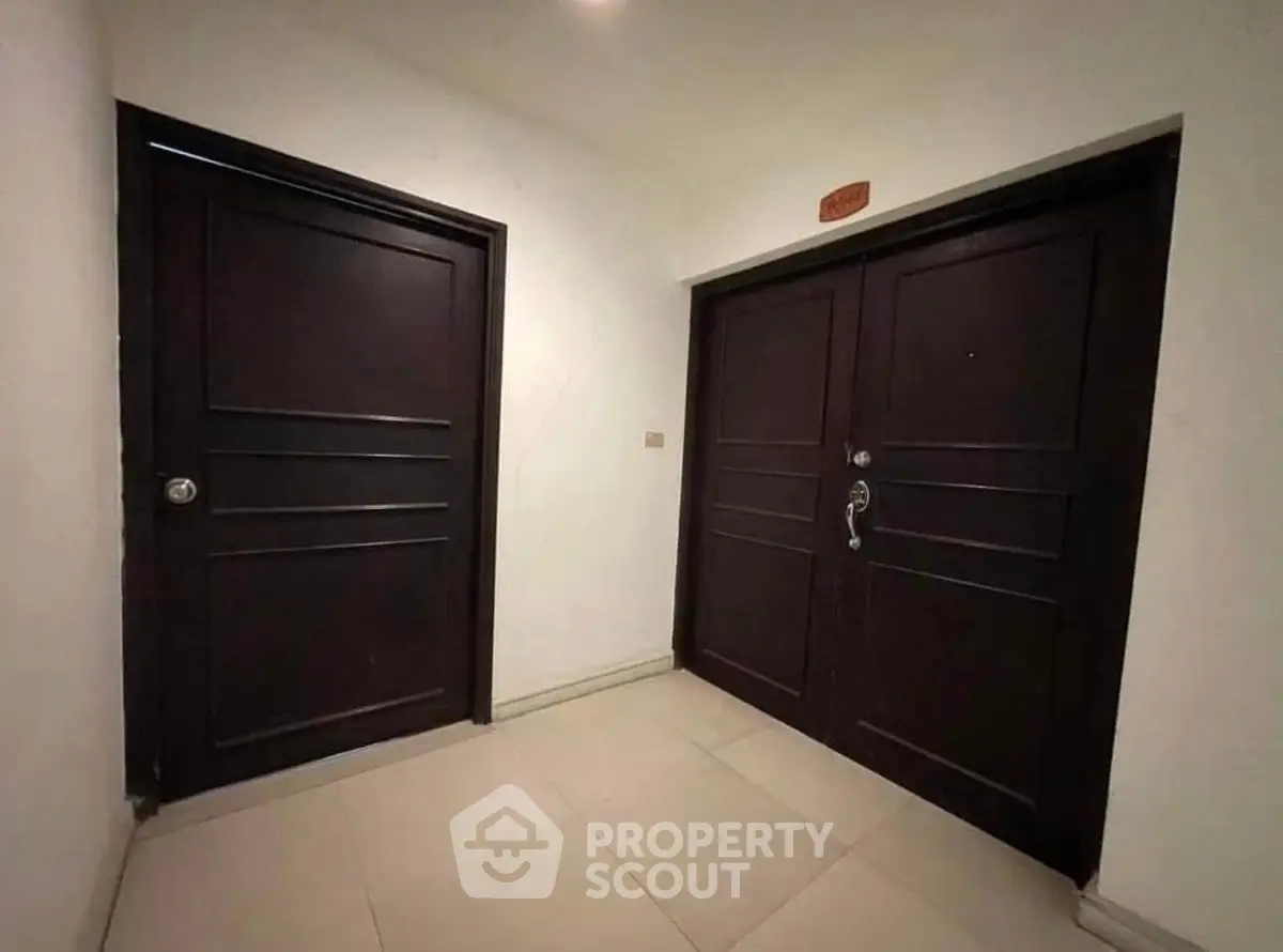Modern apartment entrance with sleek dark wood doors and tiled flooring.