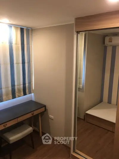 Cozy bedroom with wooden flooring, mirrored wardrobe, and a study desk under striped curtains.