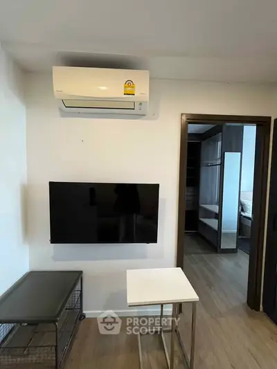 Modern living room with wall-mounted TV and air conditioning, featuring sleek furniture and wooden flooring.