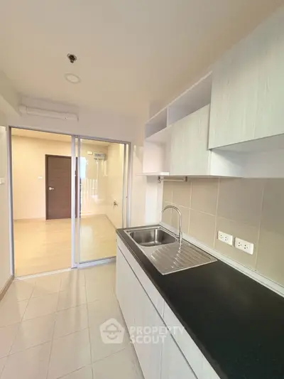Modern kitchen with sleek cabinetry and sliding glass door in a bright apartment.