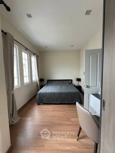 Spacious bedroom with wooden flooring and ample natural light from large windows.