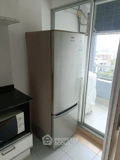 Modern kitchen with sleek fridge and microwave near balcony with city view.