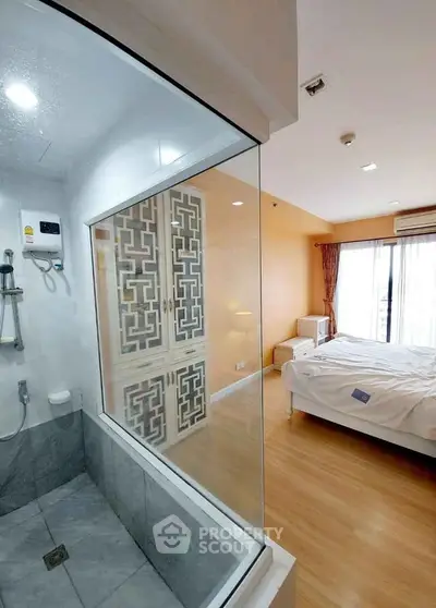 Modern bedroom with glass partition to bathroom, featuring elegant decor and natural light.
