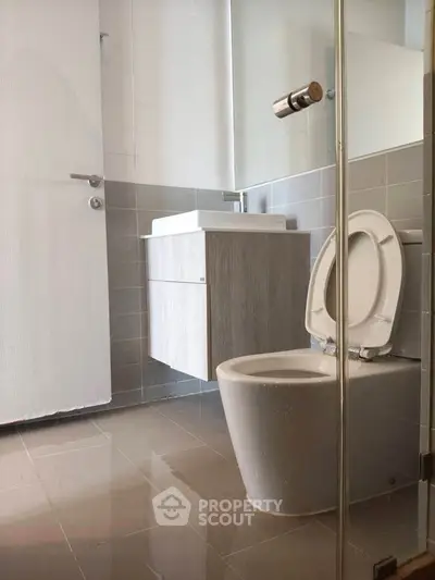 Modern bathroom with sleek fixtures and neutral tiles, featuring a floating vanity and glass shower enclosure.