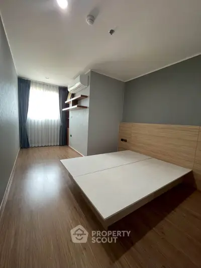 Spacious bedroom with modern design and wooden flooring, featuring a built-in air conditioner and large window.