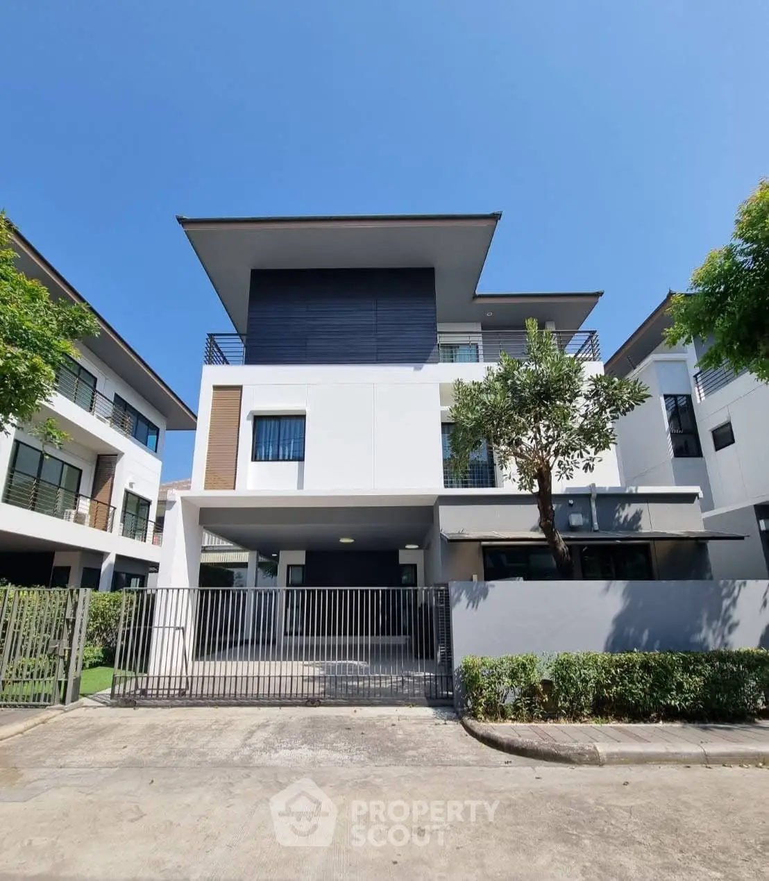 Modern three-story house with sleek design and spacious balcony under clear blue sky.